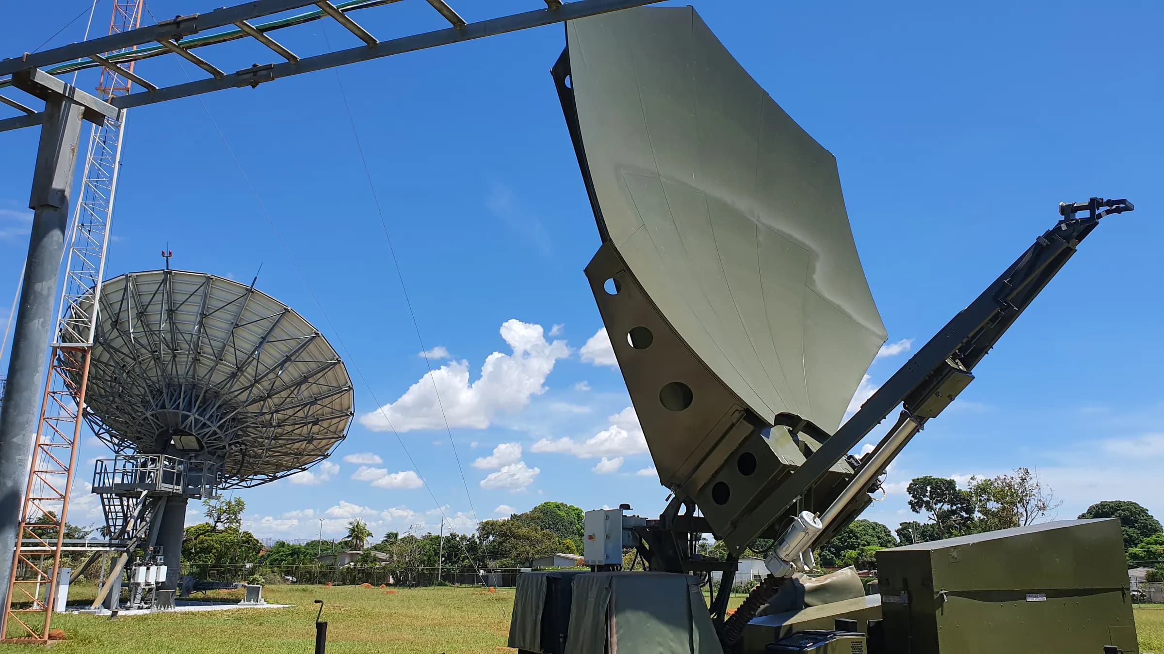 Antena SATCOM movel posicionada em campo aberto, com antena parabolica de grande porte ao fundo