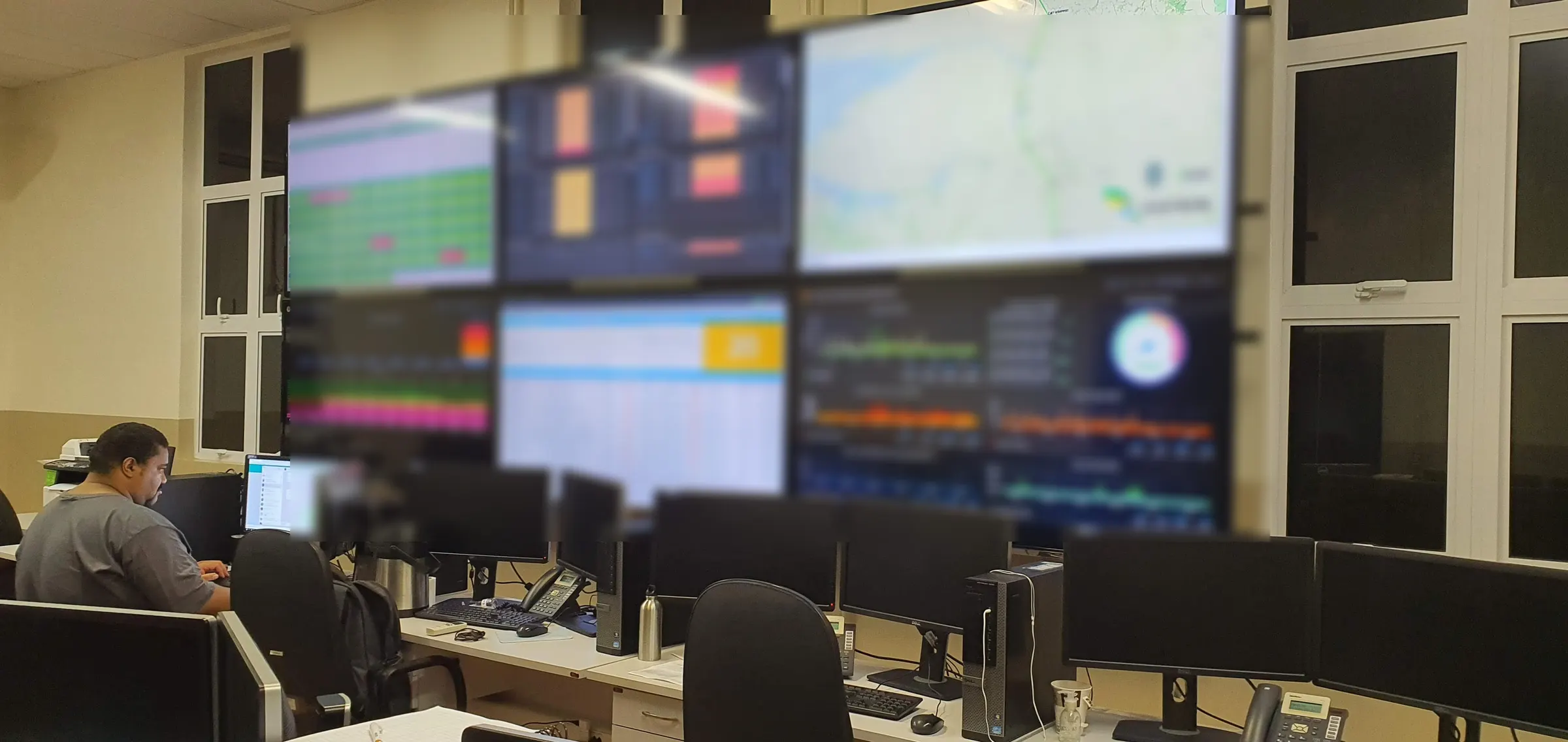 Sala de operacao com video wall de paineis de monitoramento e operador acompanhando a rede